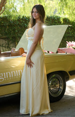 Side view of a yellow satin maxi dress showing the low scoop back with tie-up spaghetti straps and subtle diagonal skirt seams
