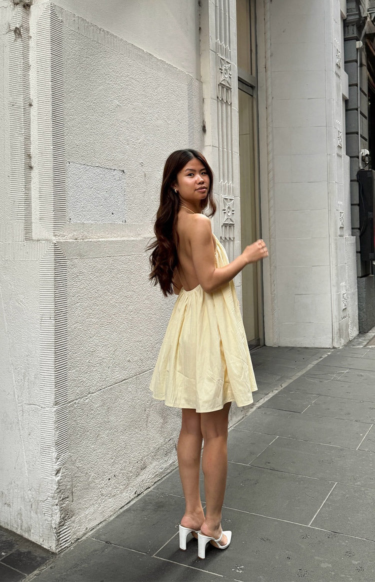 Rear view of a yellow halter mini dress with a low open back and gathered skirt