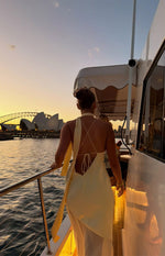 Rear view of a yellow satin maxi dress with a low scoop back, criss-cross tie straps, and a long scarf detail