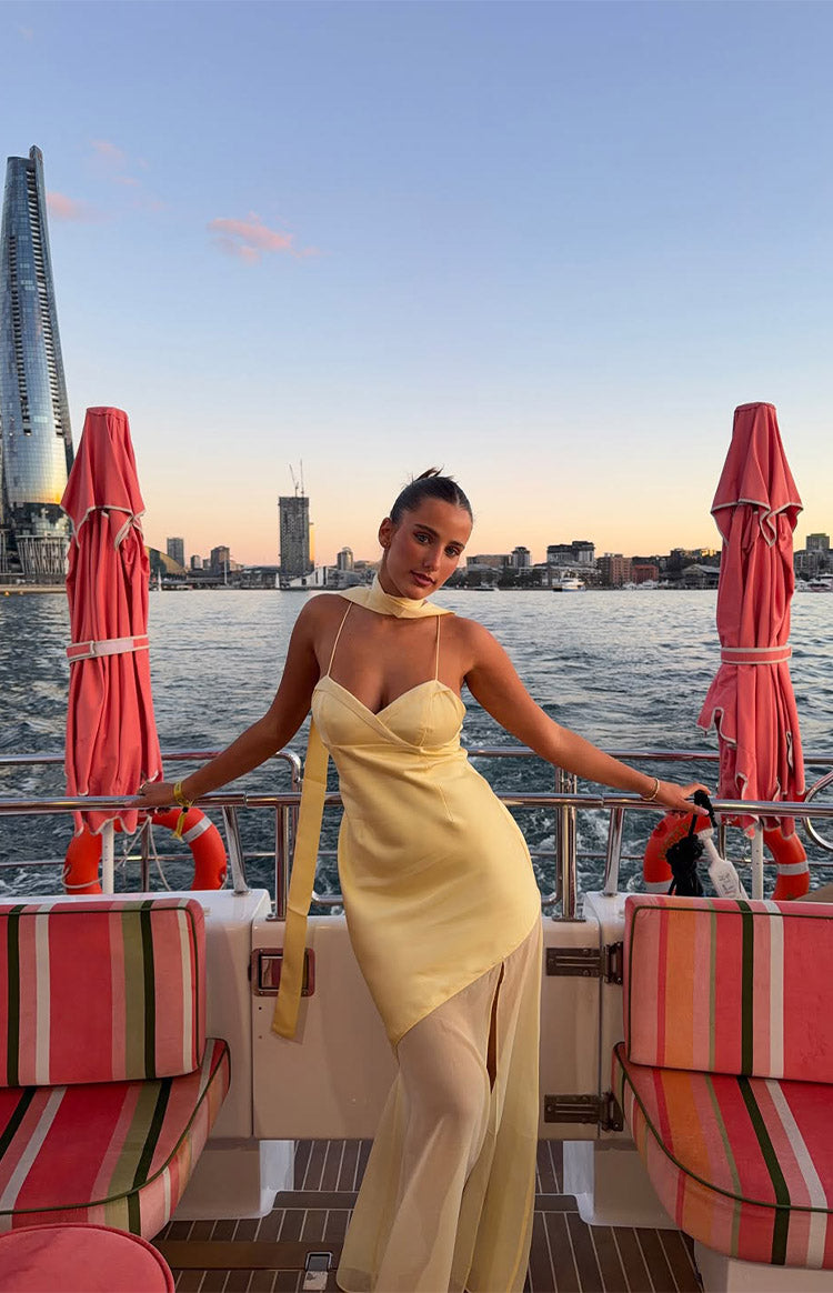 Yellow satin cowl neck maxi dress with thin straps, a long draped scarf, and a sheer panel skirt with a high slit