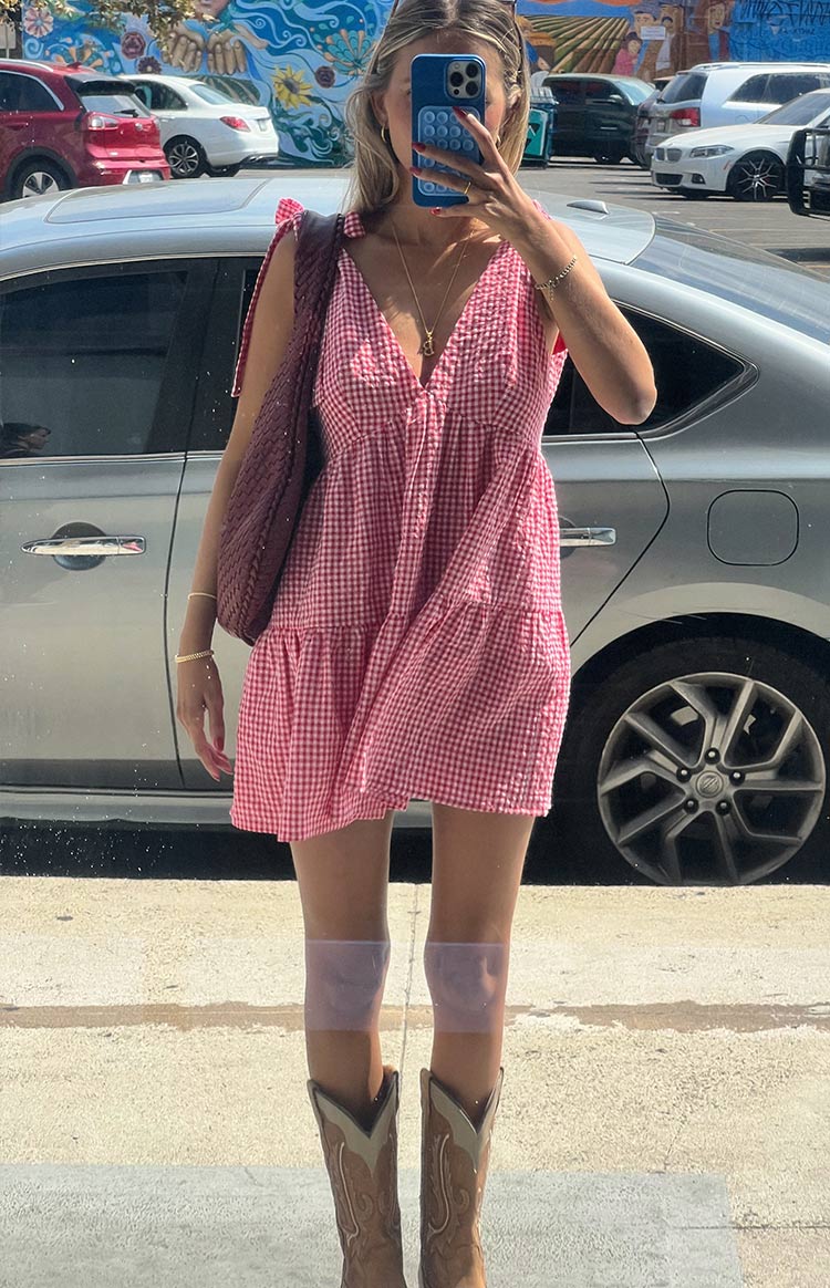 Front view of a red gingham mini dress featuring a V-neckline, tie-up shoulder straps, and a tiered skirt