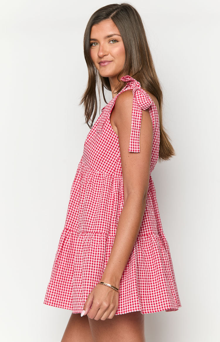 Side view of a red gingham mini dress with shoulder tie straps and a tiered skirt