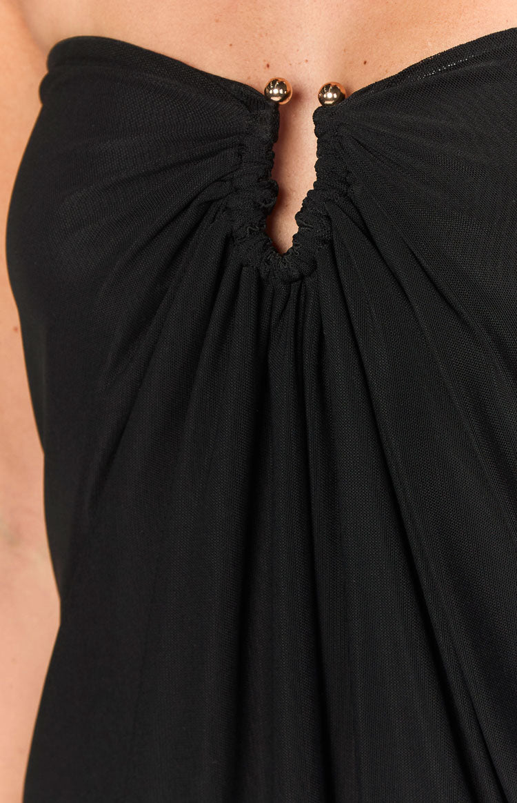 Close-up of the ruched strapless neckline of a black mini dress with a central keyhole and two gold beads