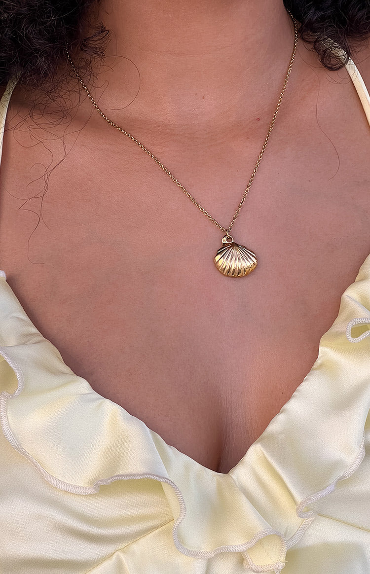 Close-up of the gold shell pendant showing its ribbed texture and the delicate gold chain