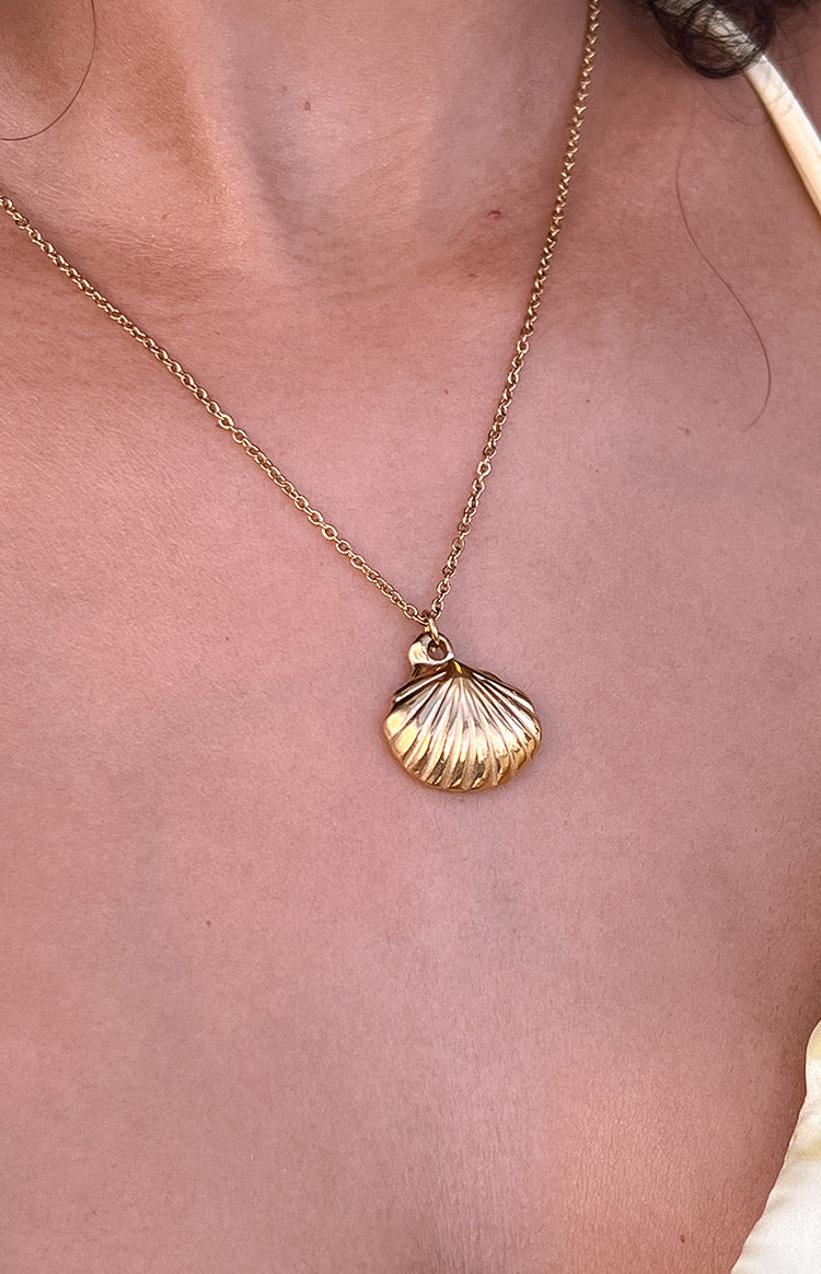 Close-up of a gold shell pendant necklace with ribbed texture on a delicate chain