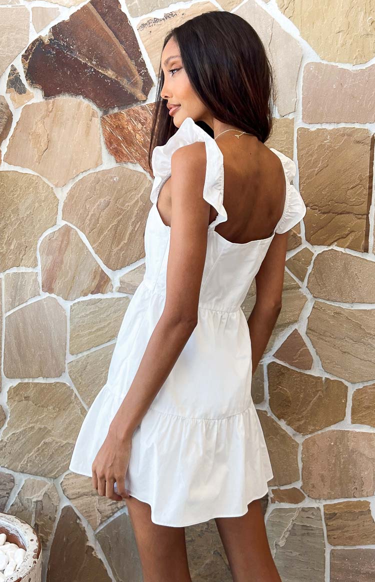Rear-side view of a white mini dress with a low square back, ruffled shoulder straps, shirred waist, and tiered skirt