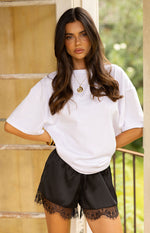 Front view of black satin shorts with delicate lace trim along the hem
