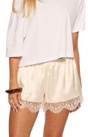Cream satin shorts with a delicate white lace hem, showing the flowy fit from the side