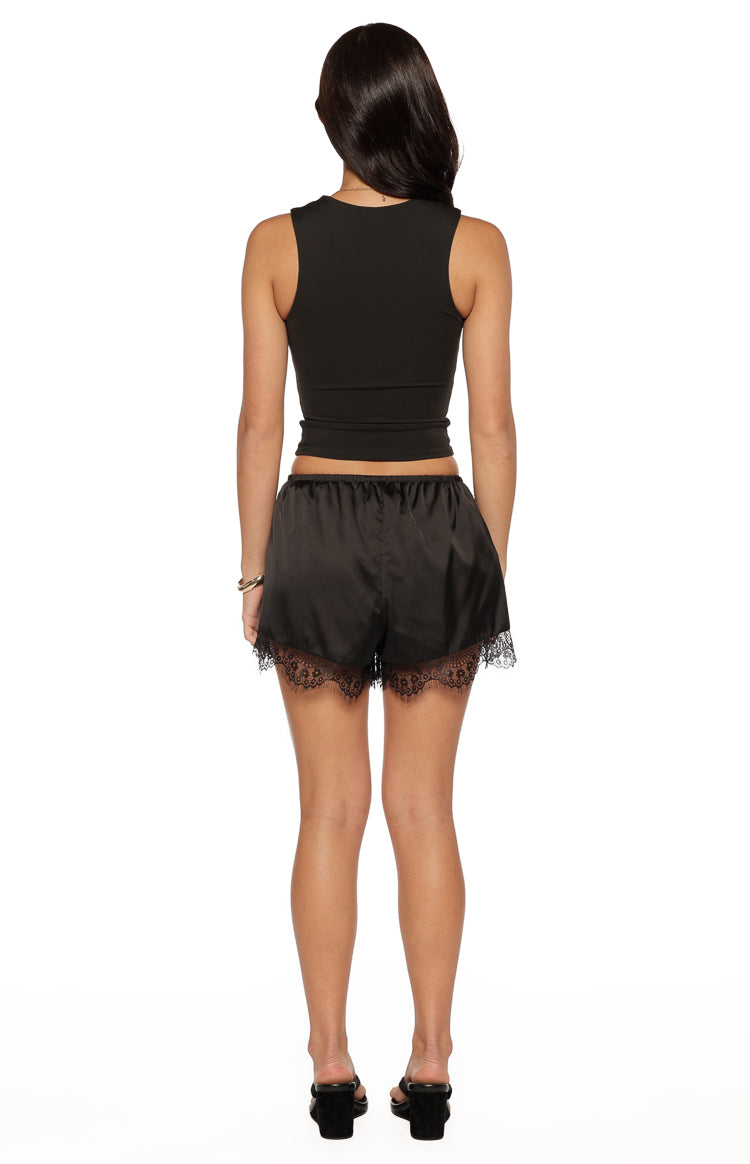 Rear view of black satin shorts with a wide elasticated waist and delicate lace trim along the hem