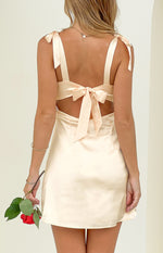 Rear view of a cream satin mini dress showing the tie shoulders, large back tie, and cutout waist