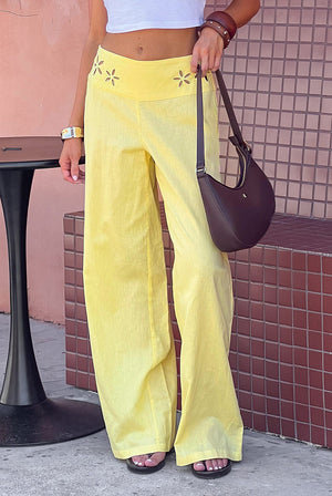Close-up of the yellow wide leg pants showing the V-shaped waistband with floral cutouts and textured fabric