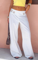 White wide-leg pants with floral cutouts on the waistband and a relaxed, flowy fit