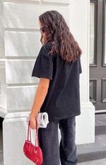 Rear view of a black oversized tee with short, loose sleeves and a relaxed, straight hem