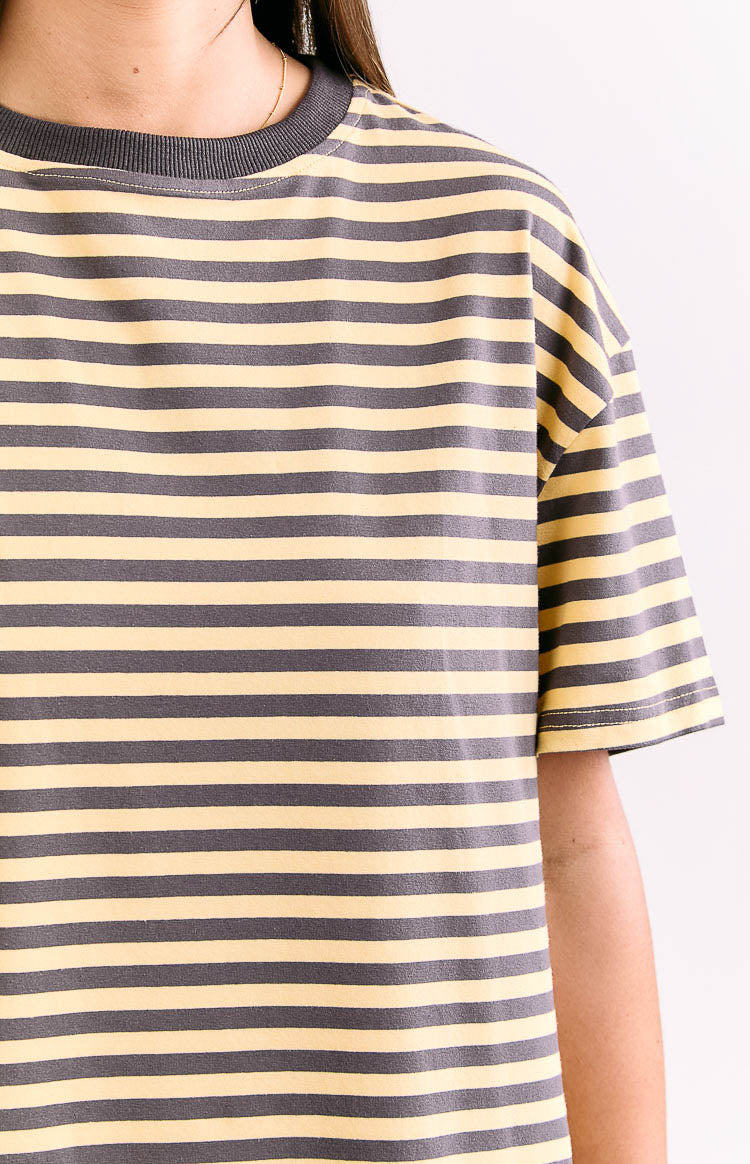 Close-up of the grey ribbed crew neck and dropped shoulder of a yellow and grey striped oversized tee