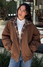 Front view of a brown puffer jacket, partially unzipped to reveal its brown plaid lining, with elasticated cuffs and hem