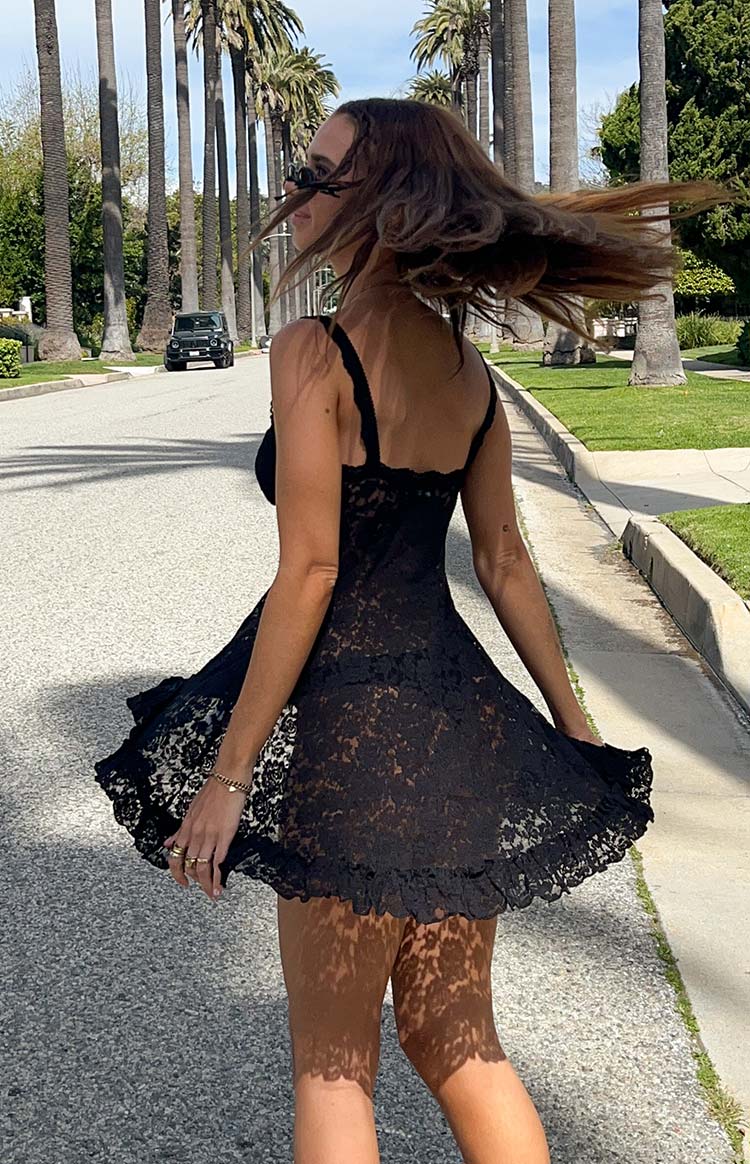 Rear view of a black sheer lace mini dress with a flared skirt and ruffled hem