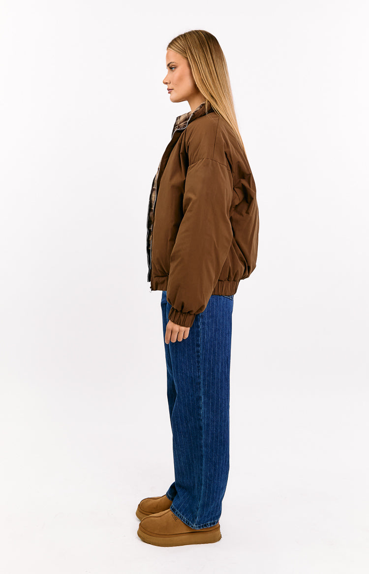 Side profile of a brown puffer jacket with a relaxed fit, elasticated waist and cuffs, and plaid collar lining