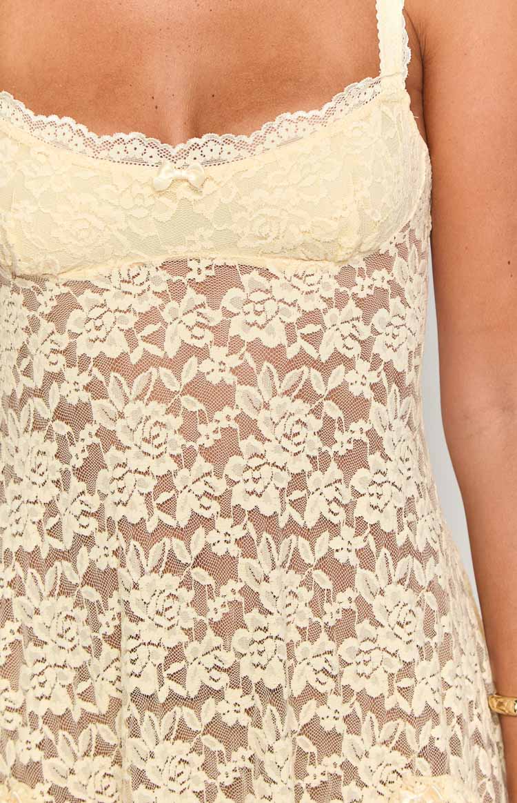 Close-up of the cream floral lace pattern on the mini dress, highlighting the scalloped neckline trim and small bow