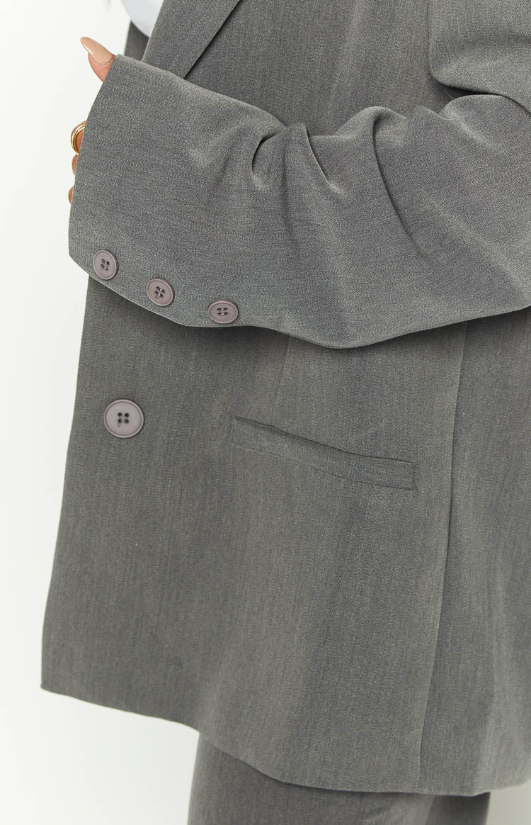 Close-up of the grey blazer's sleeve cuff with three buttons, a single front button, and a flap pocket