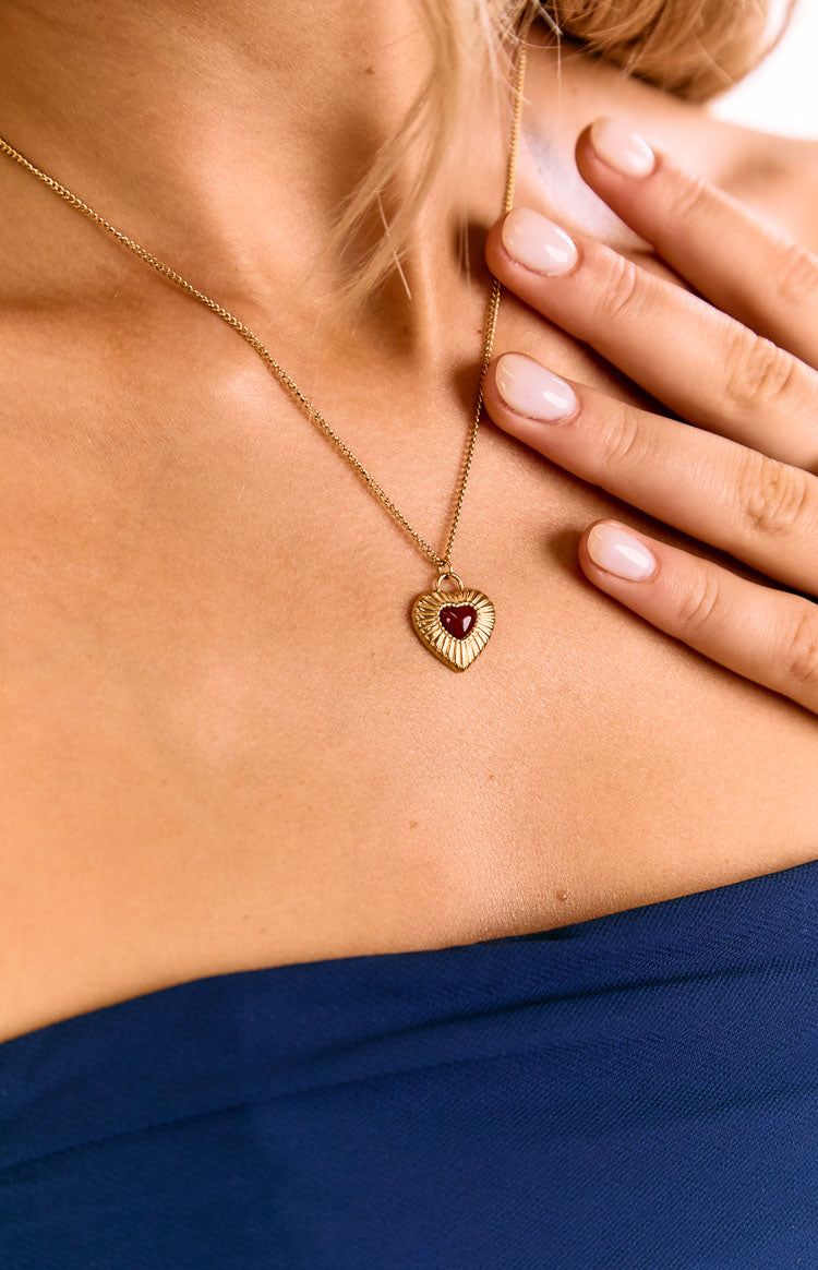 Close-up of a gold chain necklace with a textured heart pendant featuring a red heart in the center