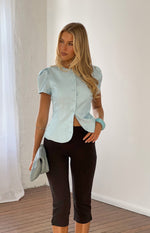 Front view of a light blue organza button up top with short puff sleeves and a curved hem