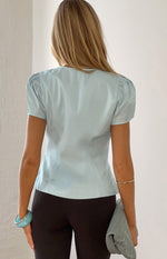 Rear view of the light blue organza top with short puff sleeves, subtle texture, and tailored back seams