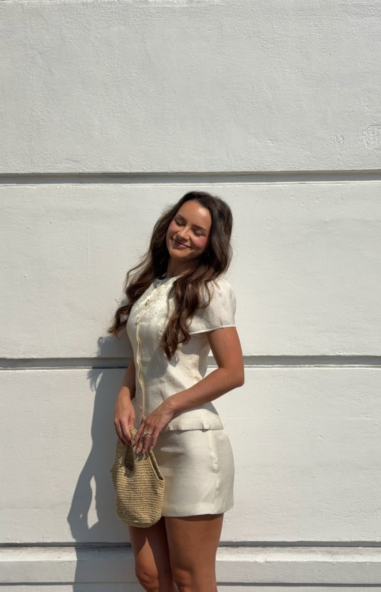 Side view of a fitted cream organza mini skirt with a smooth texture and short hemline