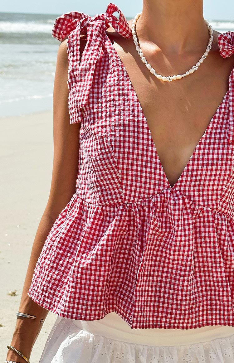 Close-up of a red gingham tie top with a deep V-neckline, tie-shoulder straps, and a gathered peplum hem