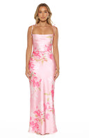 A full-length studio shot of oum model wearing a floor-length pink satin-style maxi dress featuring a large-scale vibrant pink floral print. This dress has thin shoulder straps that tie at the top a draped cowl-style neckline and asymmetrical ruching across the hip and midsection.