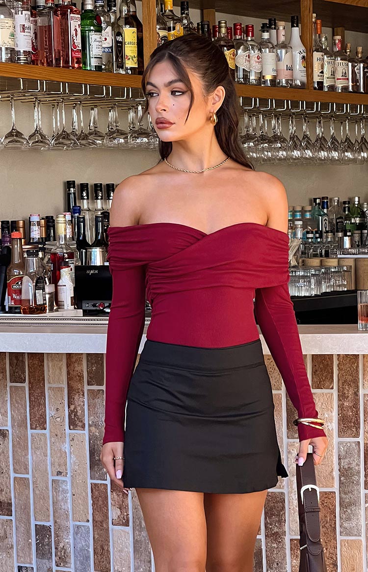 Fitted red off-shoulder bodysuit featuring a twisted sweetheart neckline and long sleeves in ribbed knit