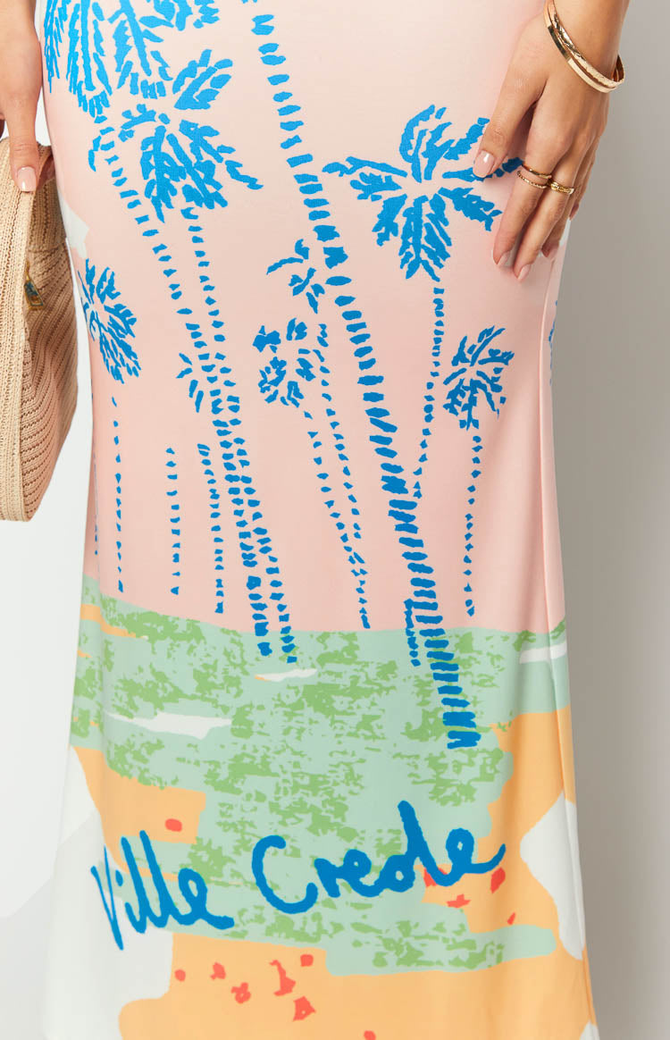 Close-up of the "Ville Crede" blue text graphic and multi-coloured abstract print on a pink palm print maxi dress