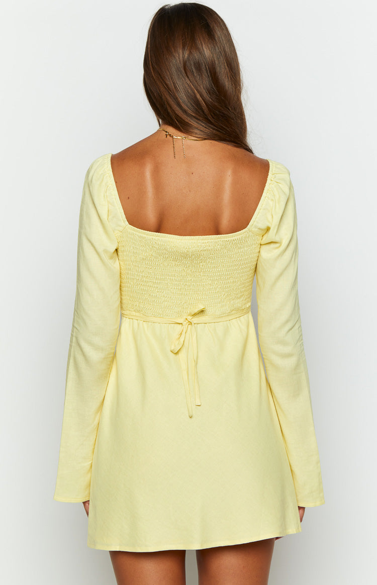 Rear view of a yellow long sleeve mini dress with a square back, smocked bodice, and tie waist detail