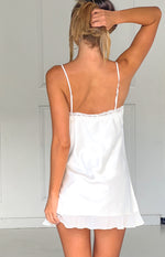 Rear view of a cream satin mini dress with thin adjustable straps, lace trim, and a ruffled hem