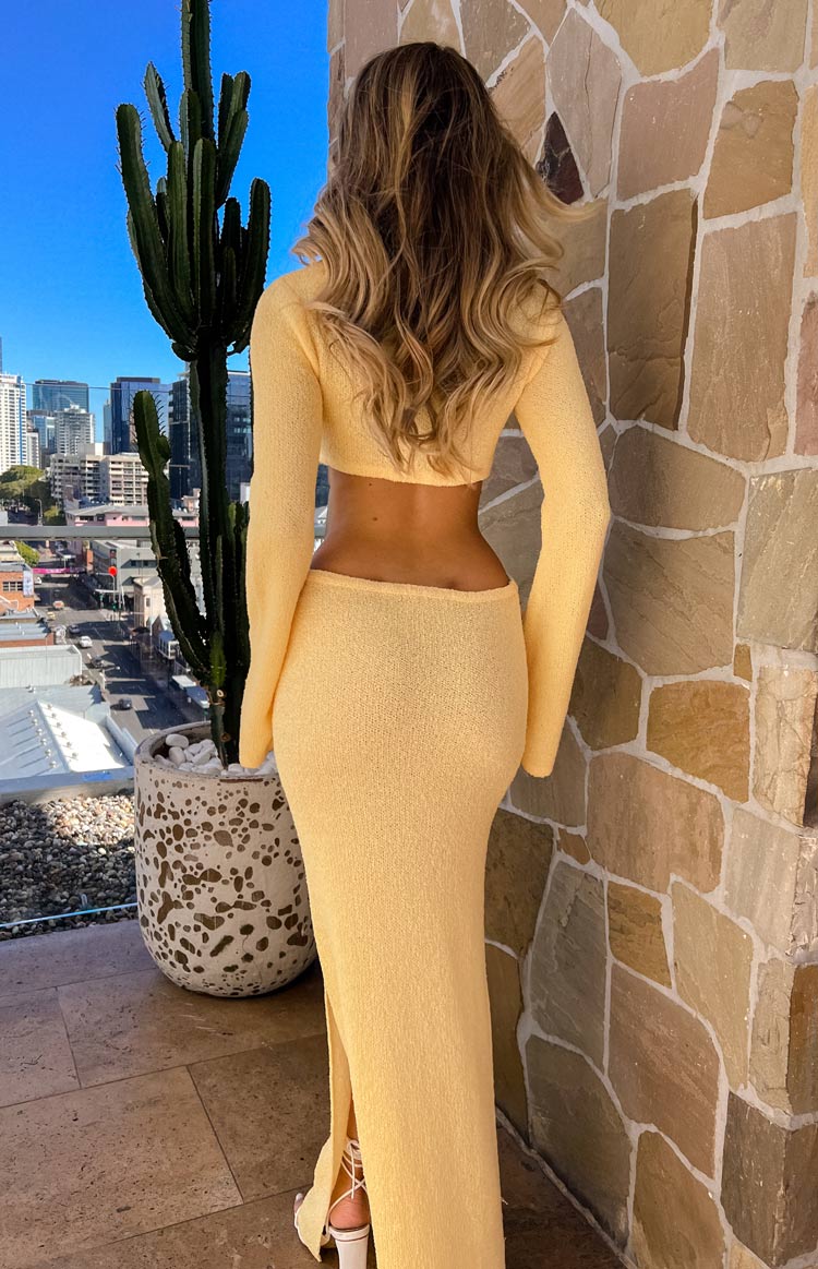 Rear view of a yellow long sleeve knit maxi dress with a mid-back cutout and side slit