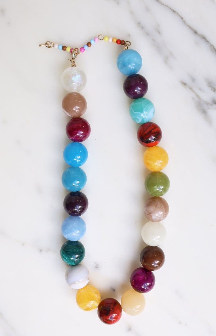 Flat lay of a multi-coloured beaded necklace with large round beads, small rainbow seed beads, and a gold lobster clasp