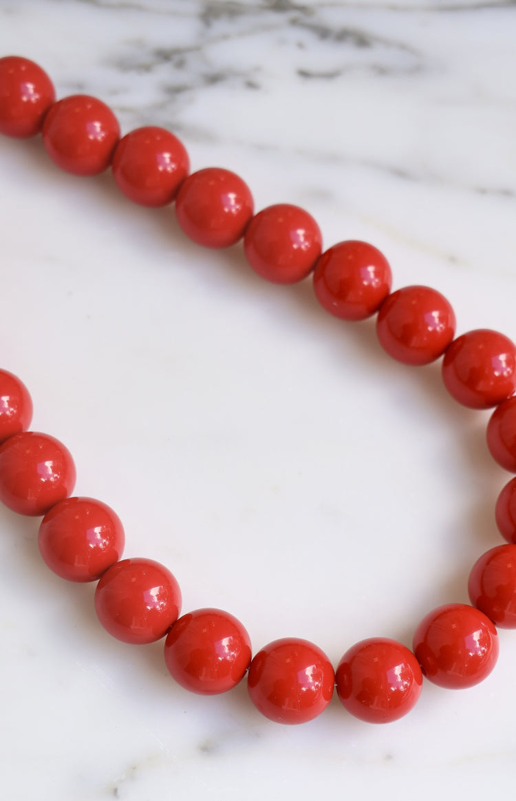 Close-up showing the vibrant red, glossy finish of the round beaded necklace