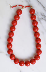 Glossy red beaded necklace with a gold lobster clasp and small red beads near the closure