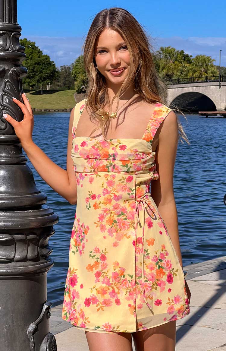 Yellow floral mini dress with a square neckline, ruched bust, and a tie-front wrap skirt detail