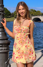 Yellow floral mini dress with a square neckline, ruched bust, and a tie-front wrap skirt detail