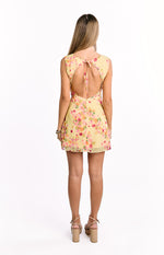 Rear view of a yellow floral mini dress with an open back, tie-back neckline, and cap sleeves