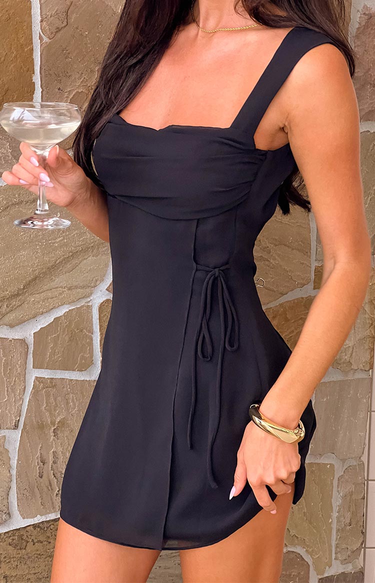 Side view of a black chiffon mini dress showing the ruched bust, wide straps, and adjustable side tie detail at the waist