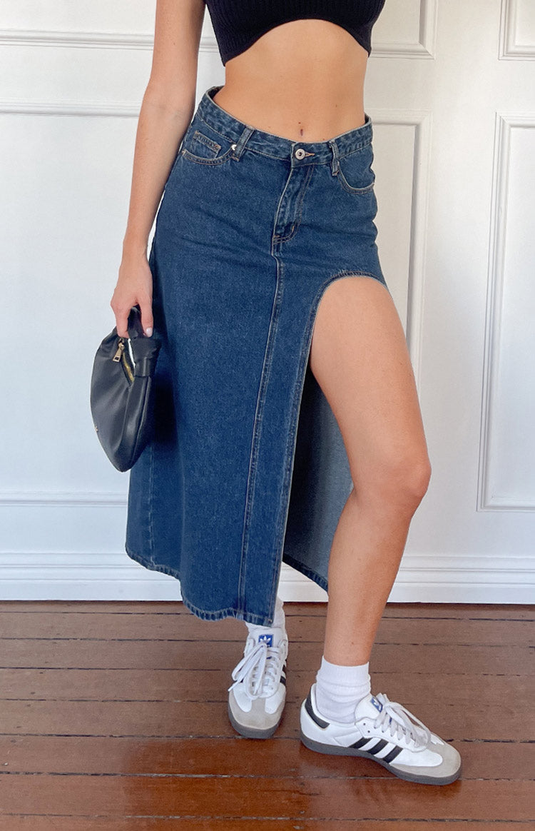 Side view of a dark wash denim midi skirt with a high left side split and a relaxed A-line silhouette