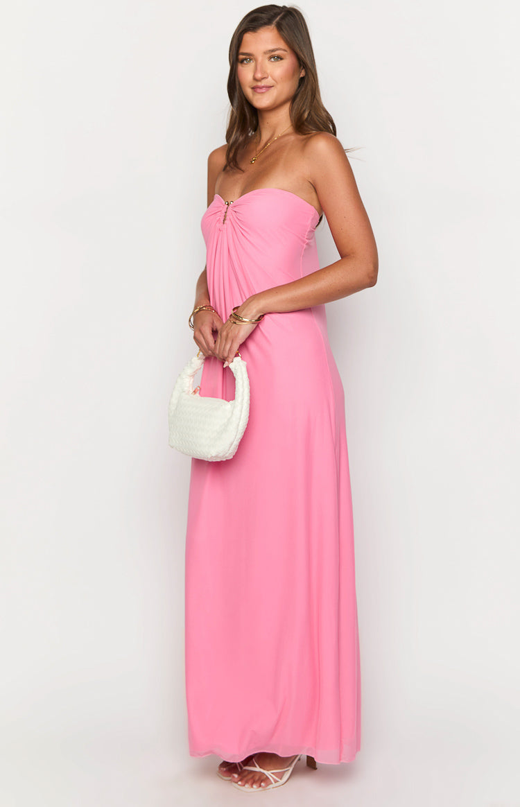 Side view of a pink strapless maxi dress with a gold ring detail at the ruched bust and a flowy skirt