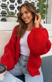 Close-up of the red chunky knit cardigan showing the oversized balloon sleeves and ribbed cuffs