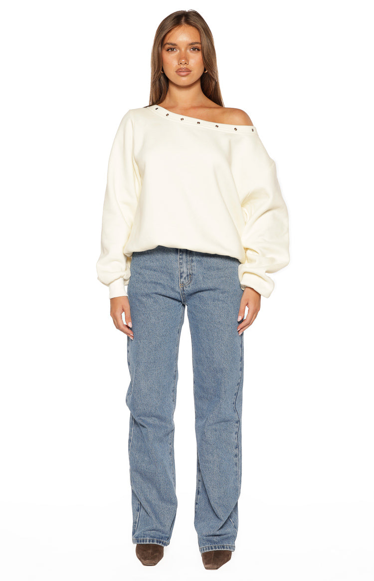 Front view of a cream oversized sweater with an asymmetric eyelet neckline worn off one shoulder