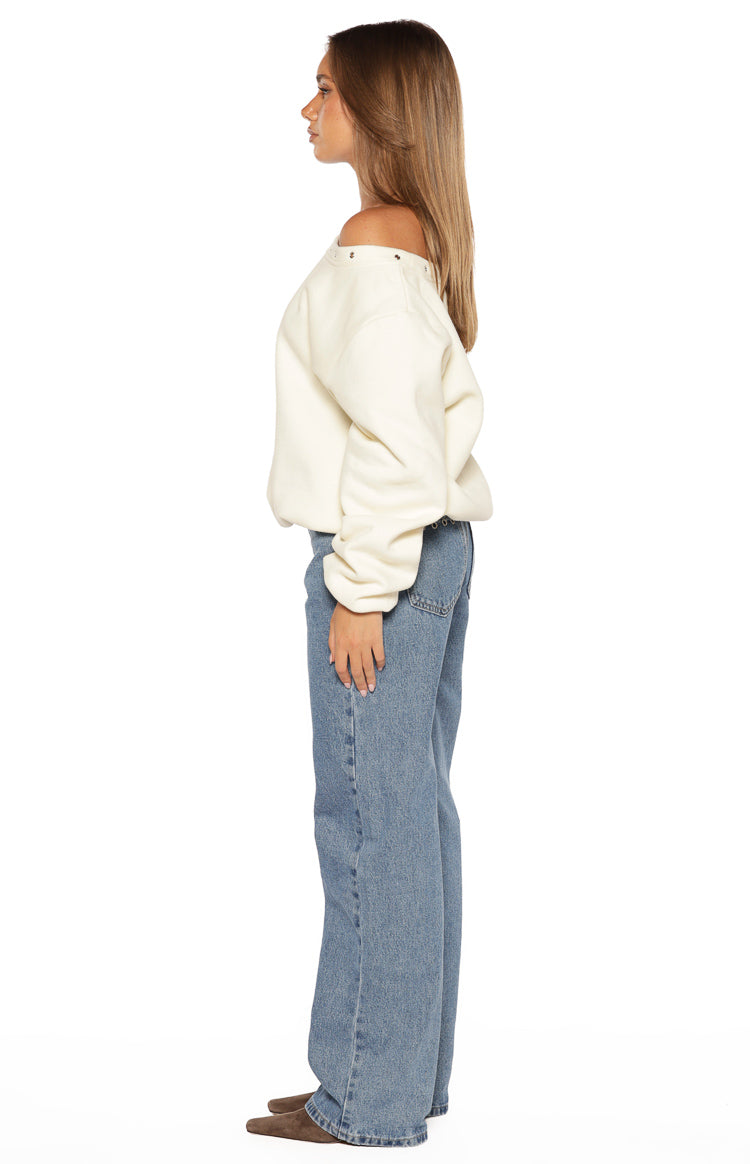 Side view of a cream asymmetric neckline sweater with eyelets and a relaxed fit