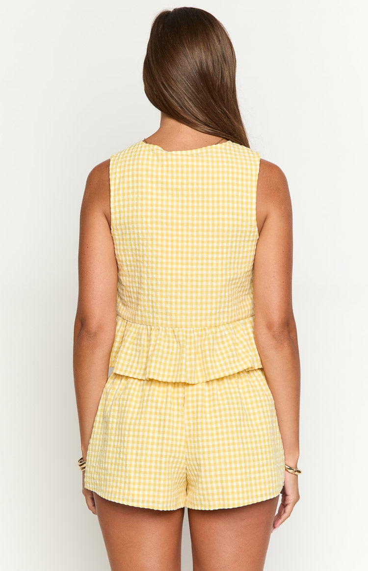 Rear view of a yellow gingham sleeveless top with a scalloped back neckline and a tiered peplum hem