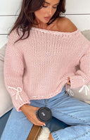 Side view of a baby pink chunky knit sweater with an off-shoulder neckline and white tie details on the cuffs and hem