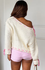 Rear view of a cream chunky knit sweater with an off-shoulder neckline and pink contrast stitching and ties