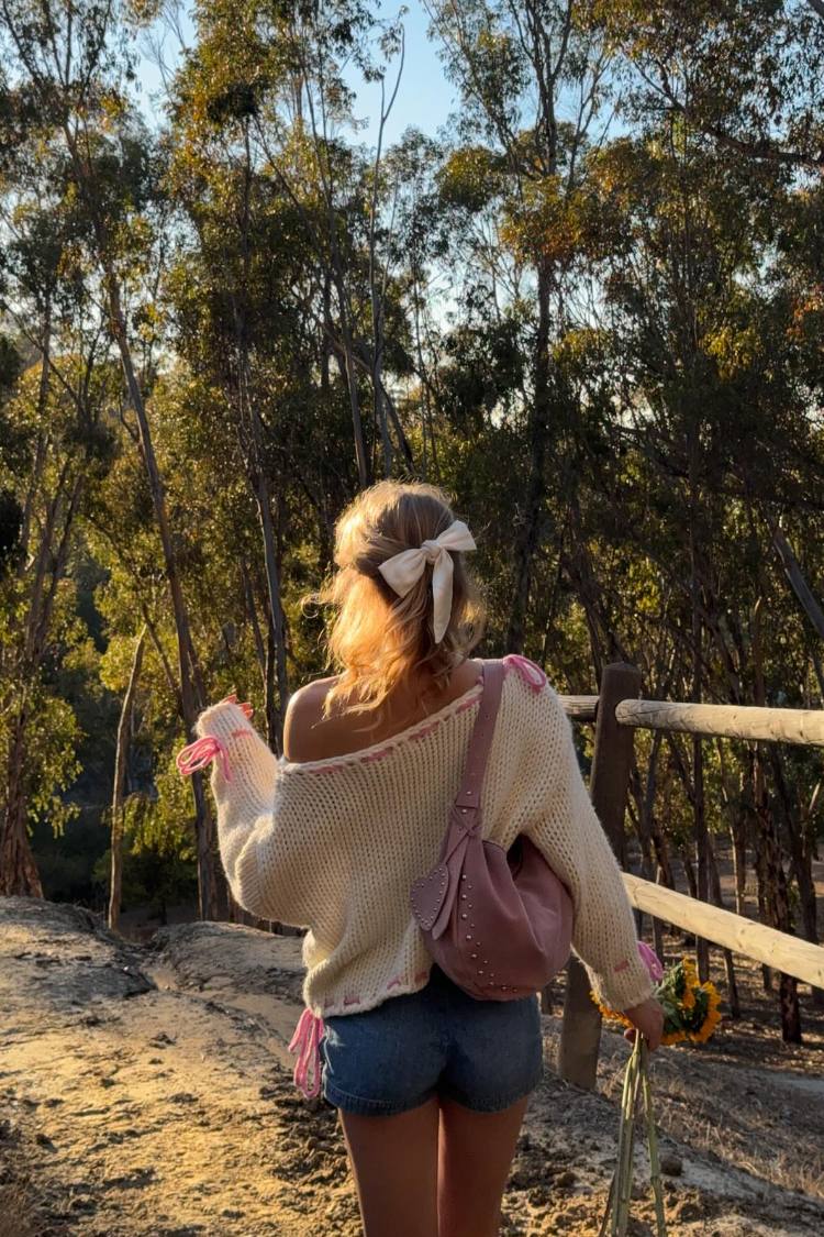 Rear view of a cream chunky knit sweater with an off-shoulder neckline and pink tie details on the sleeves and hem